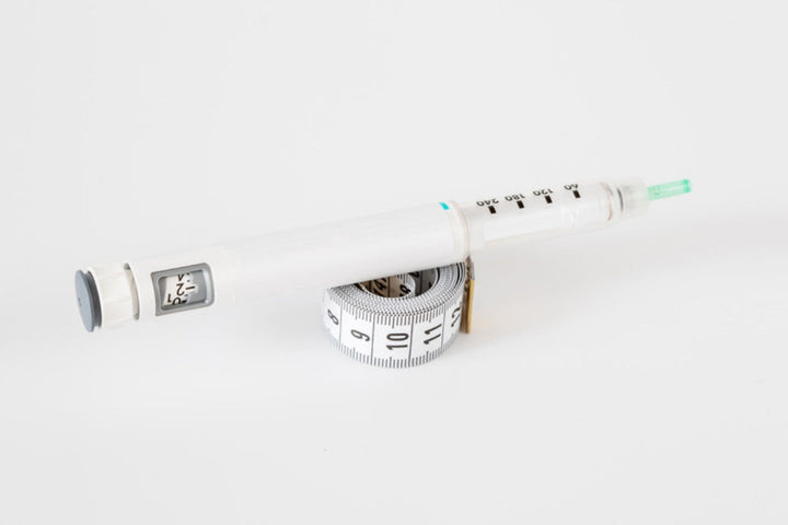 Weekly injection pen resting on a measuring tape